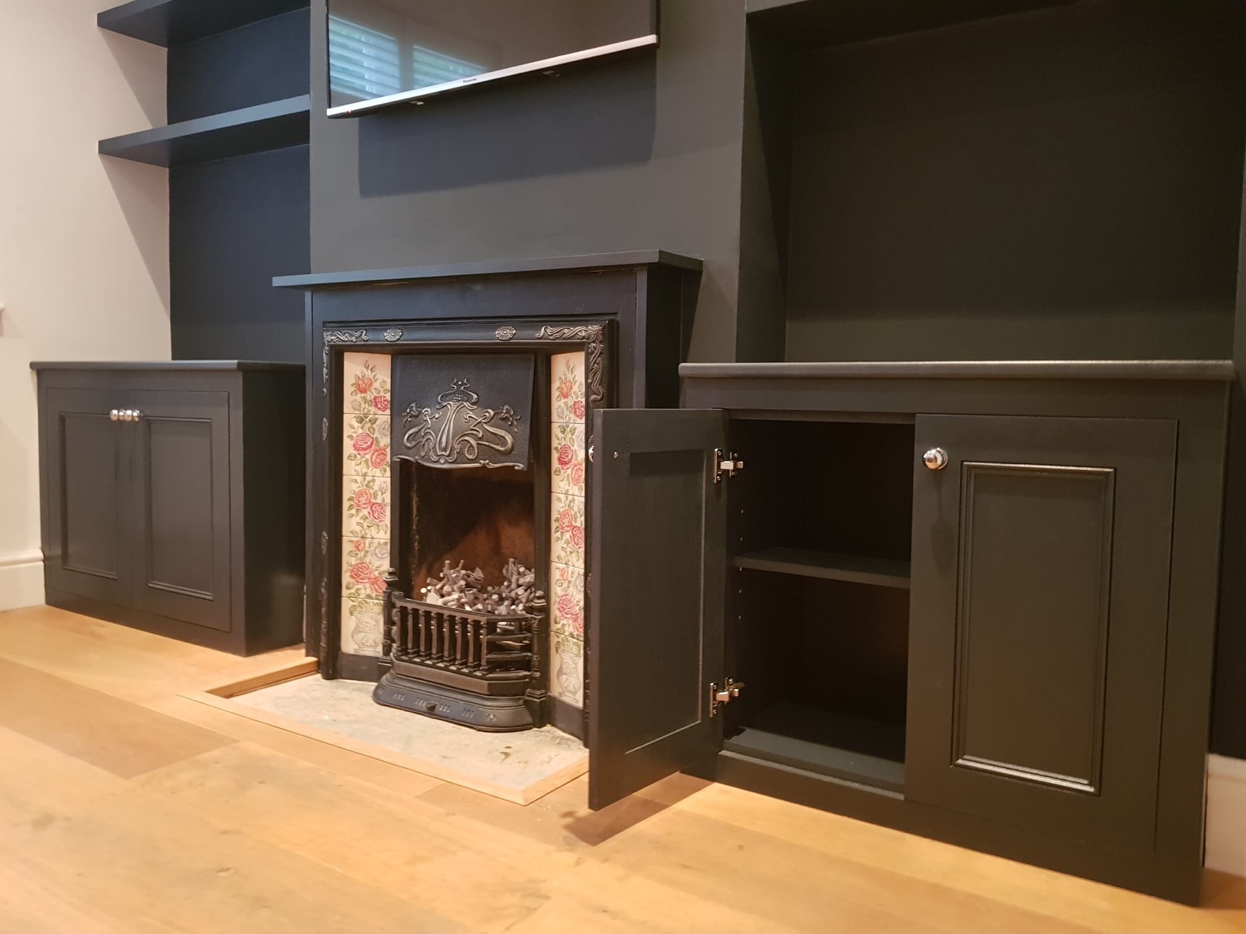 Matte-black alcove cupboards and shelves flanking a period fireplace