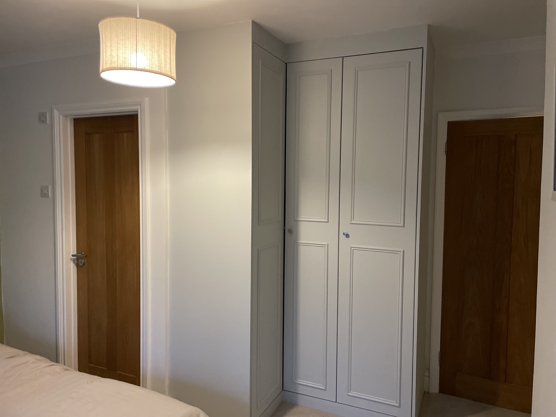L-shaped fitted wardrobe wrapping a bedroom corner in dove grey